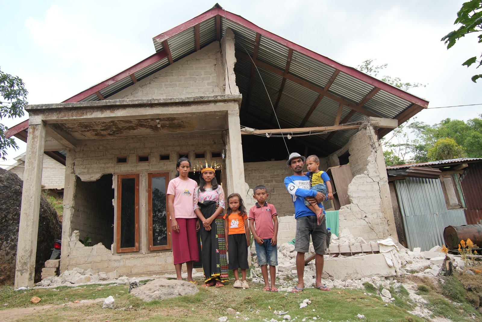 Prili's family in front of their earthquake-damaged home